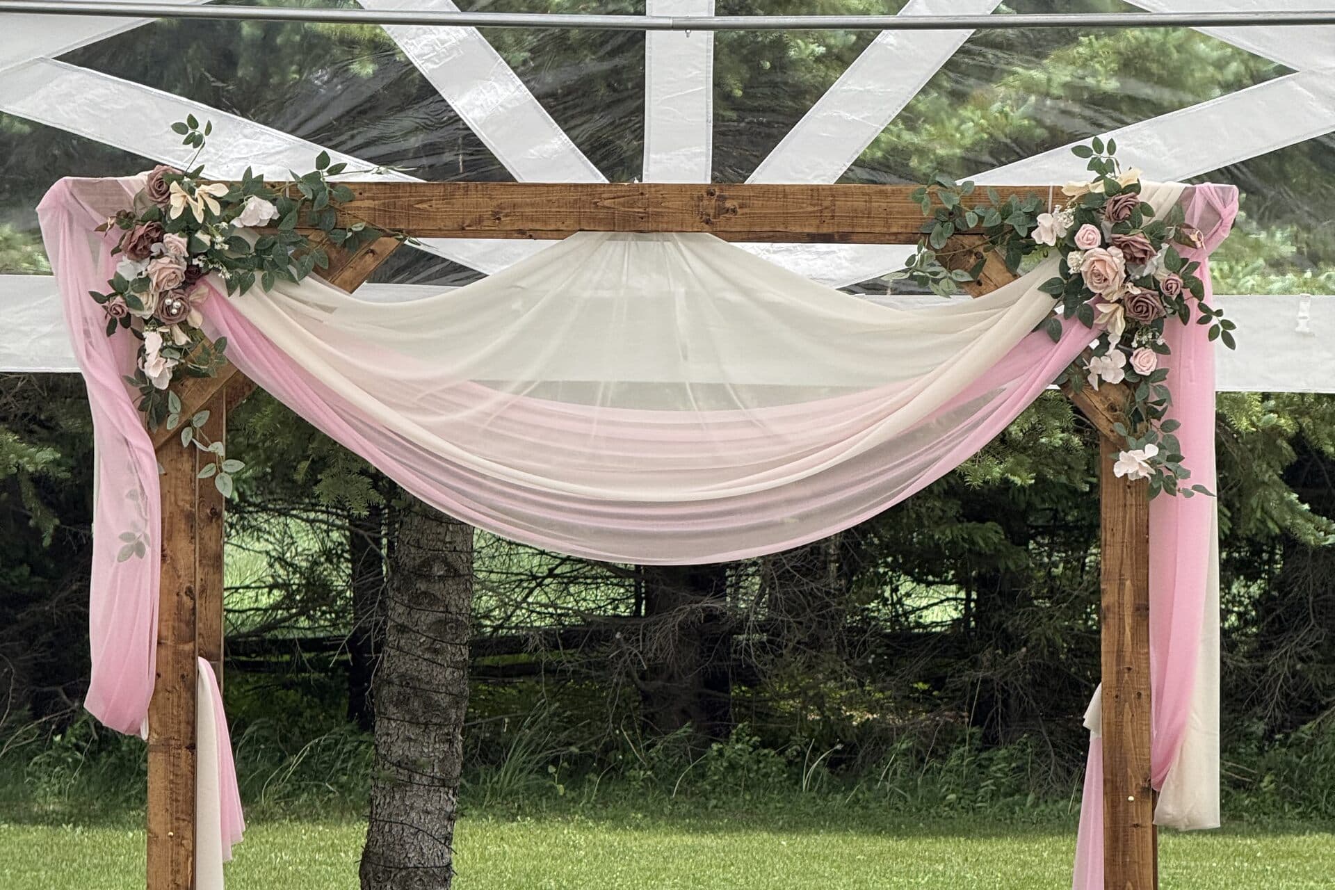 Wooden ceremony arch draped in rose and ivory fabric with floral accents beneath the tent frame