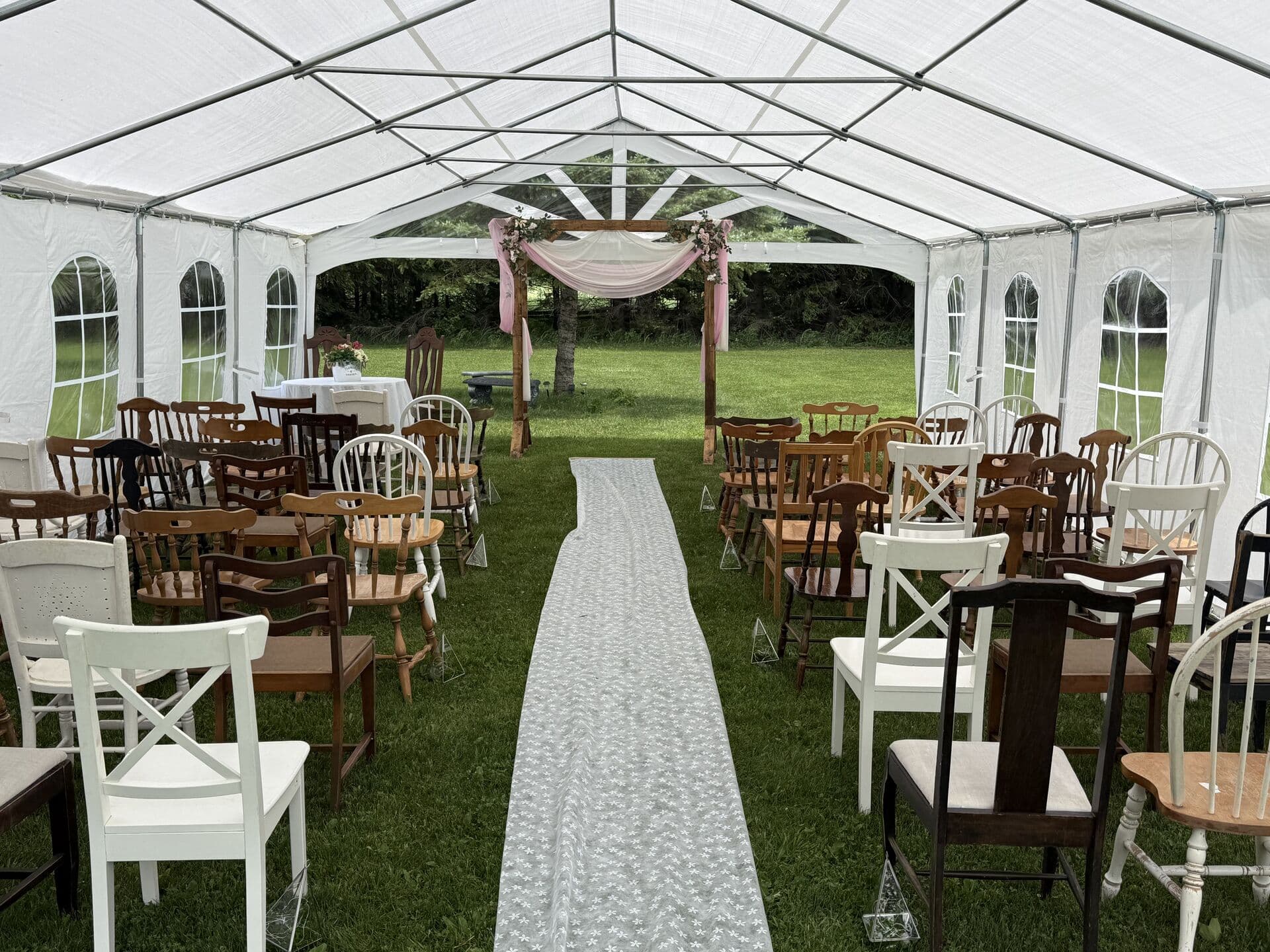 Bright tent interior set for a ceremony with an aisle and greenery beyond