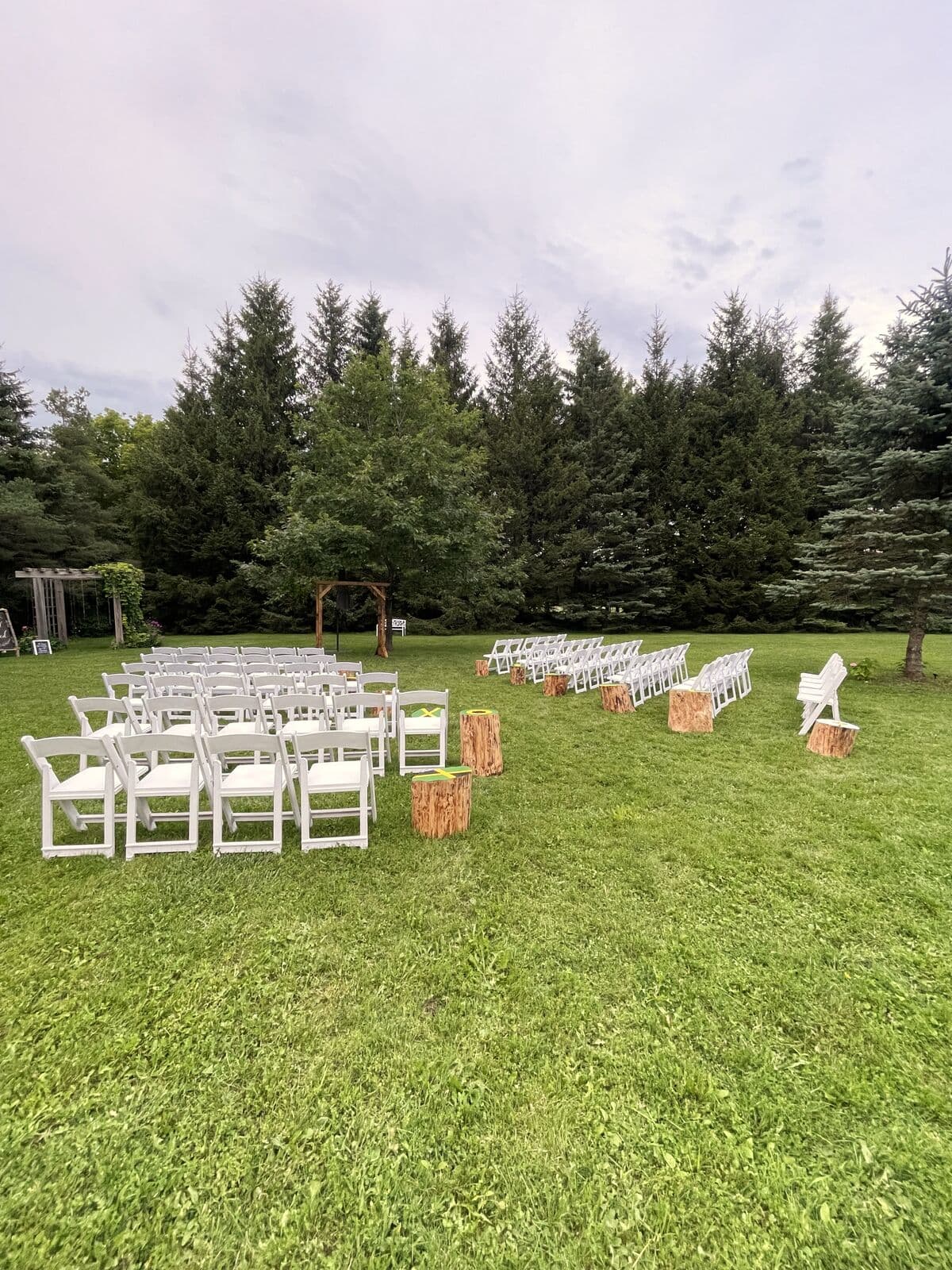 Rows of white ceremony chairs on the lawn framed by evergreens