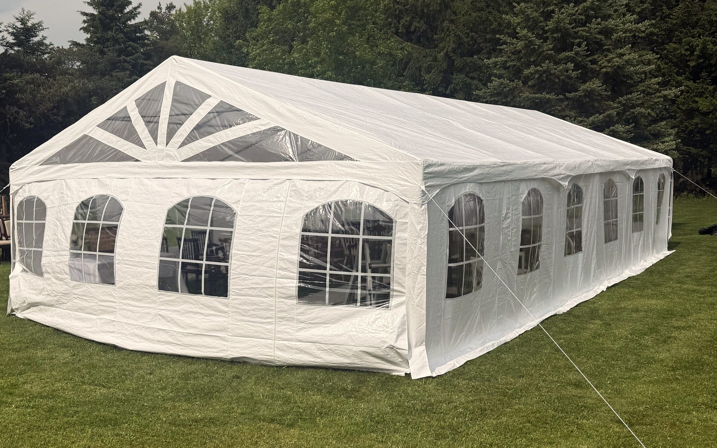 White frame tent with arched windows set on the lawn in front of tall evergreens