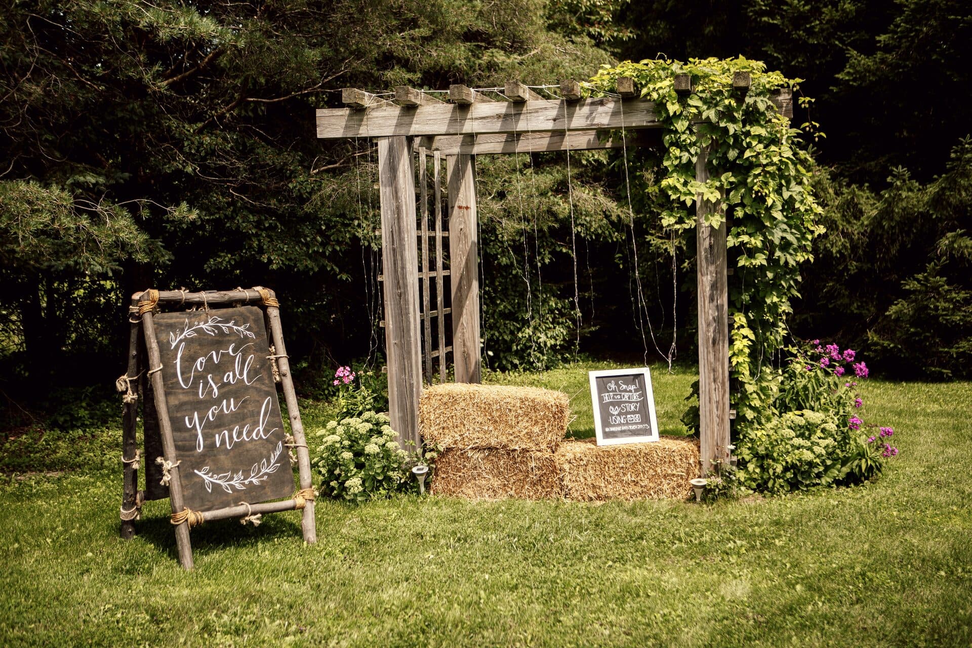 Ivy-covered pergola with a hand-lettered sign and hay-bale seating in the garden