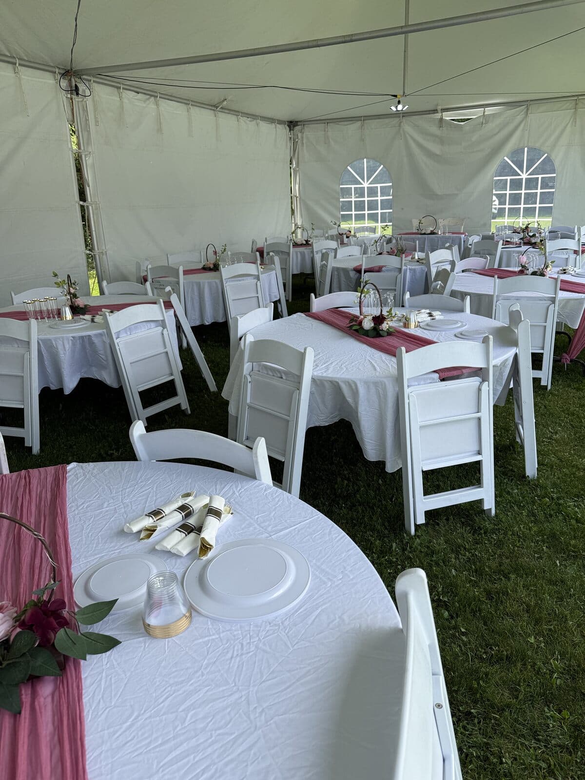 Round reception tables with white linens and rose runners inside an event tent