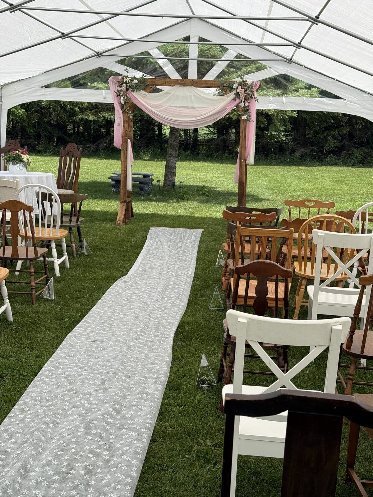 Ceremony aisle with a lace runner leading to a rose-draped arch inside an event tent